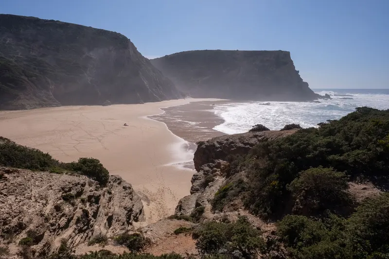 Praia da Murração — A arriba central é de xisto negro riscado por veios vermelhos e laranja, e a vegetação das
