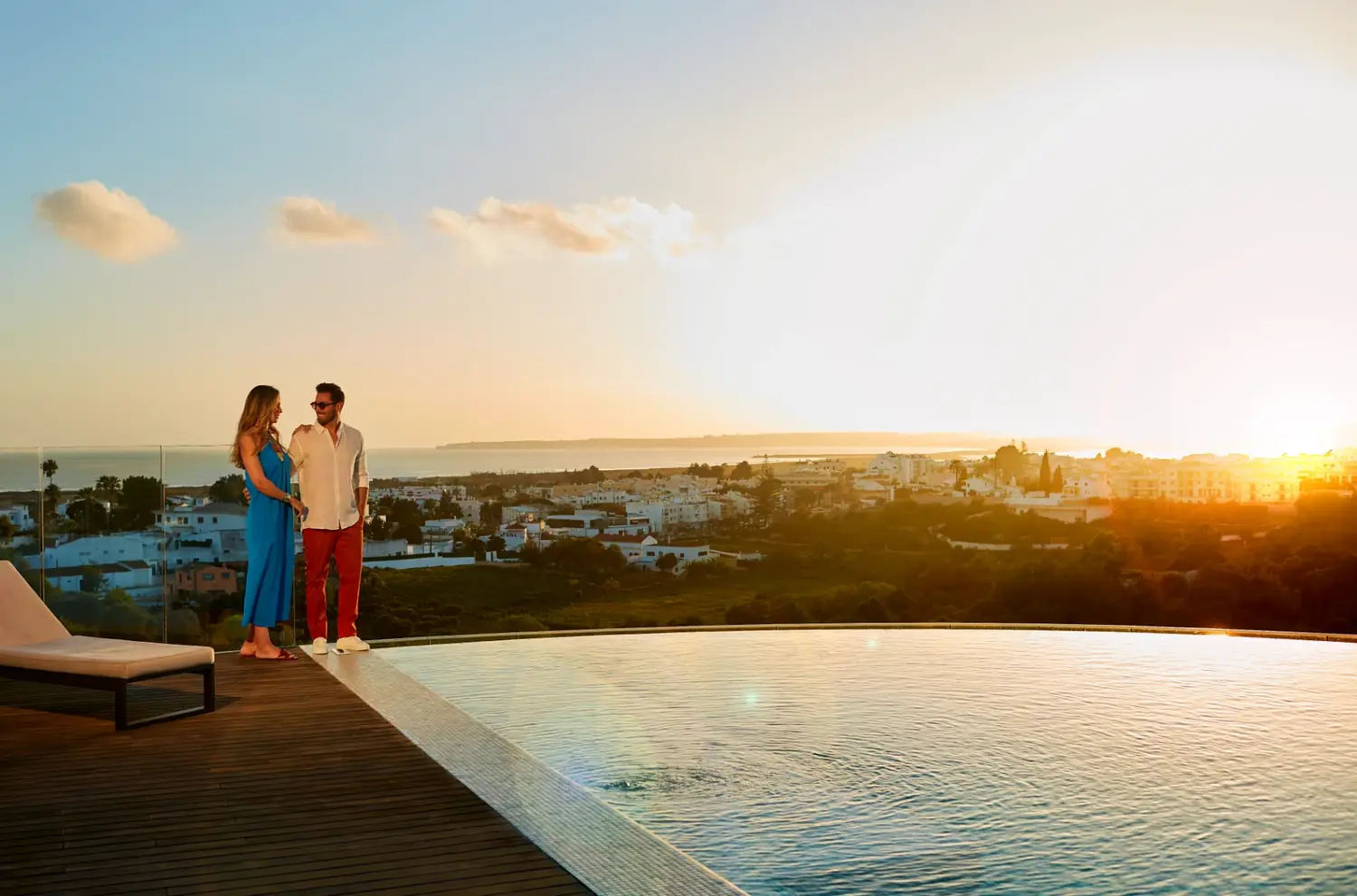 Casal ao pôr do sol no terraço do hotel, junto à piscina infinita, com Alvor ao fundo