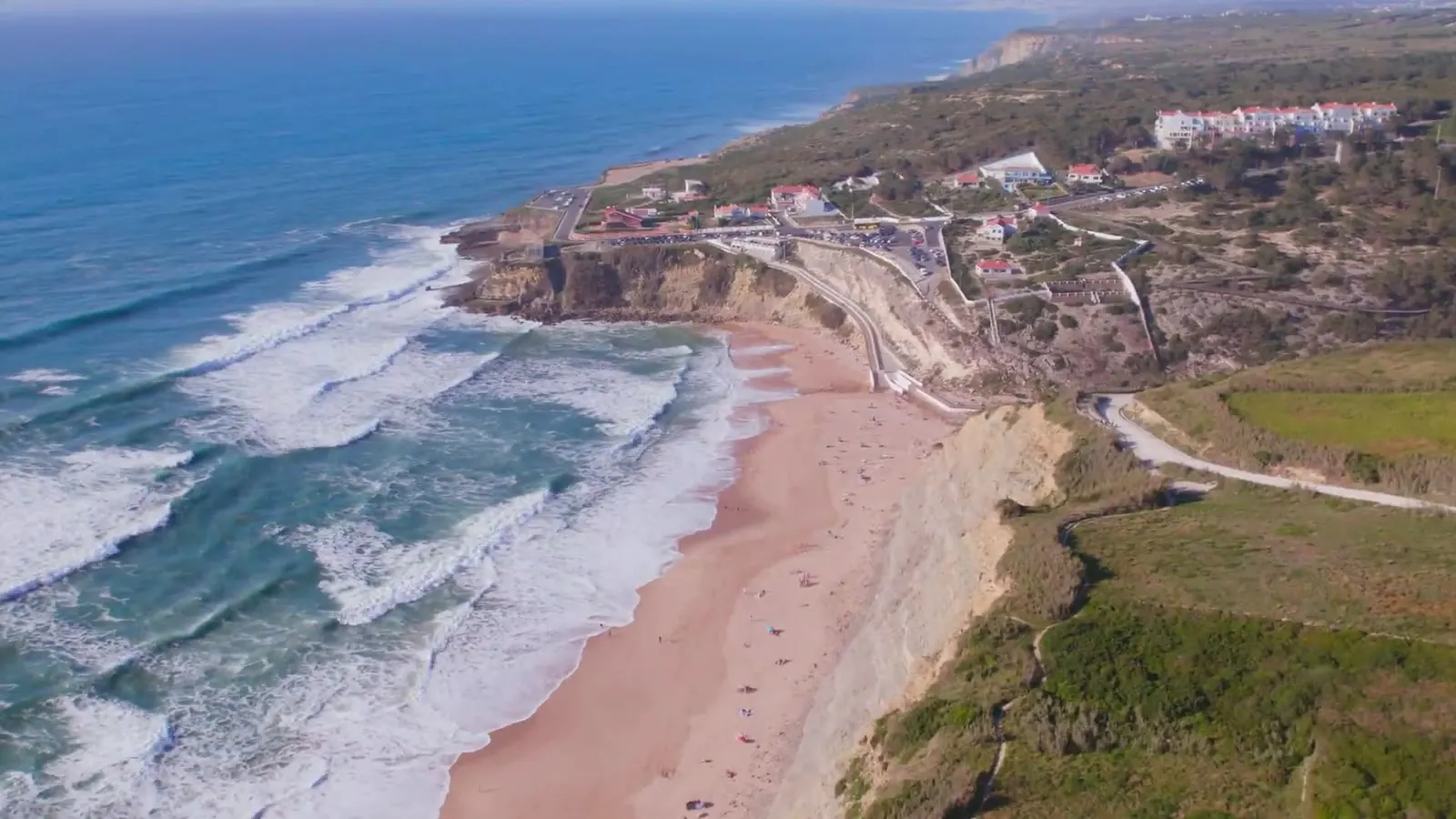 Vista aérea de uma praia larga na costa atlântica, com ondas a rebentar